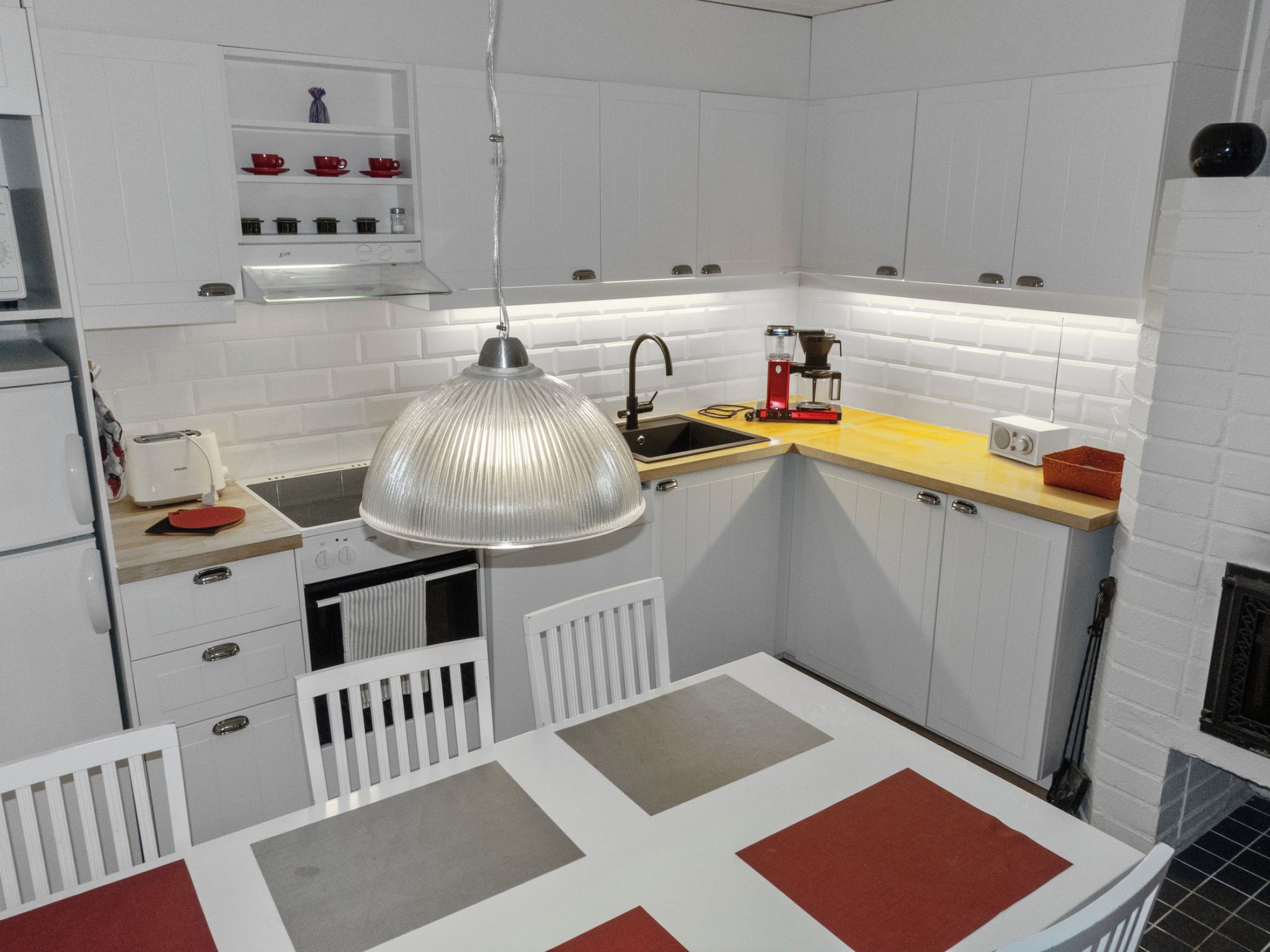 Een compacte keuken met witte kastjes, een hangende lamp, een koffiezetapparaat en een broodrooster.