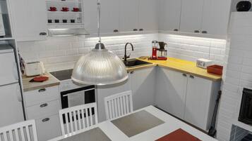 Een compacte keuken met witte kastjes, een hangende lamp, een koffiezetapparaat en een broodrooster.