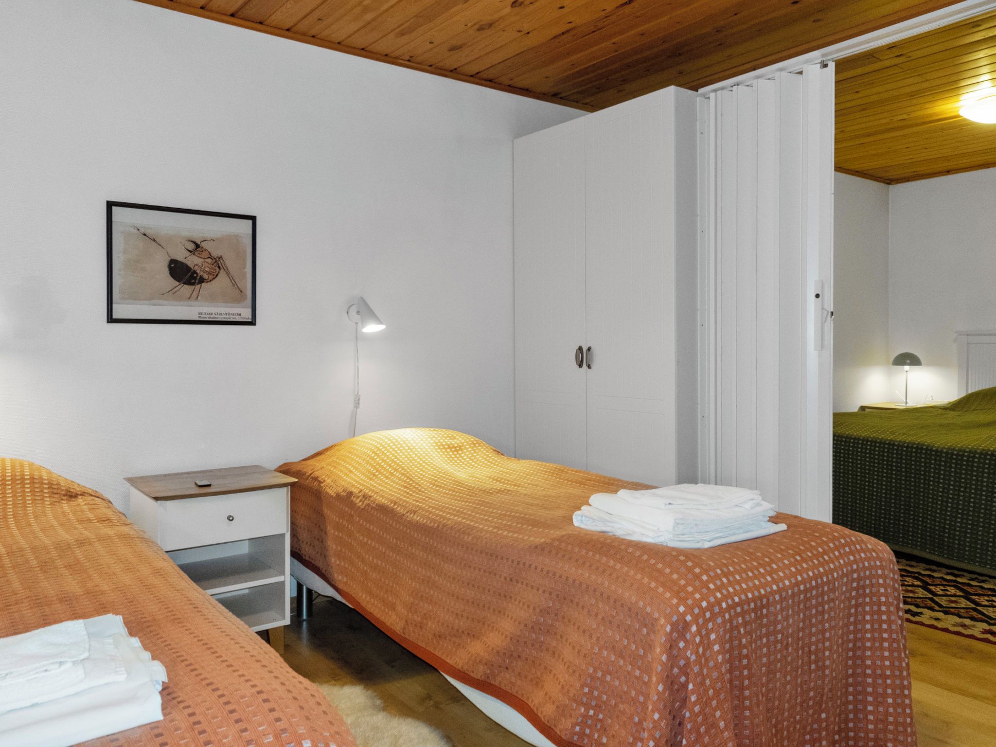 Une chambre avec deux lits, une table de chevet, un tableau encadré et une porte donnant sur une autre pièce.