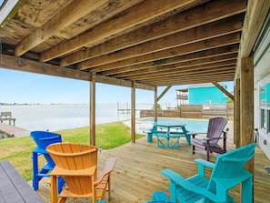 A wooden deck with outdoor seating, overlooking a body of water. - Going Coastal by Miss Kitty’s (Rockport)
