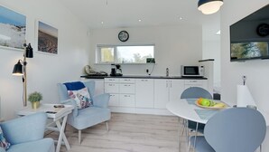 A modern kitchen with white cabinets, a dining table with chairs, a coffee machine, and a TV mounted above the counter.