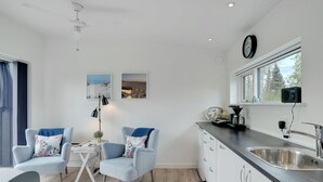 A modern kitchen with a sink, cabinets, and a window. There are two chairs and a small table with a lamp.