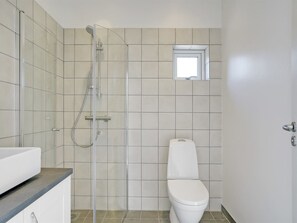 A bathroom with a shower, toilet, and a small window.