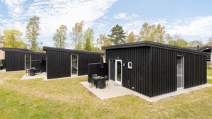 A row of black wooden cabins with outdoor seating areas and a grassy lawn.