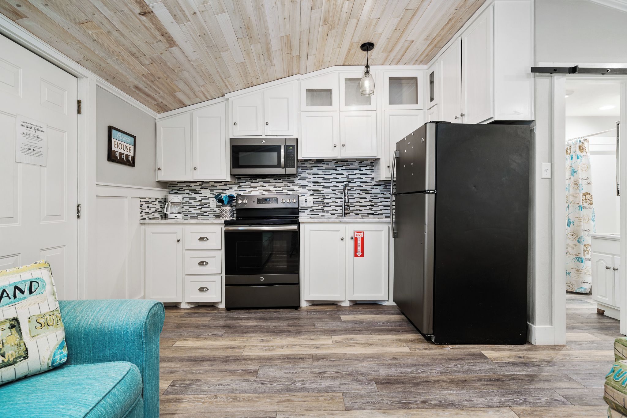 A modern kitchen with white cabinets, a black refrigerator, a microwave, and a tiled backsplash.