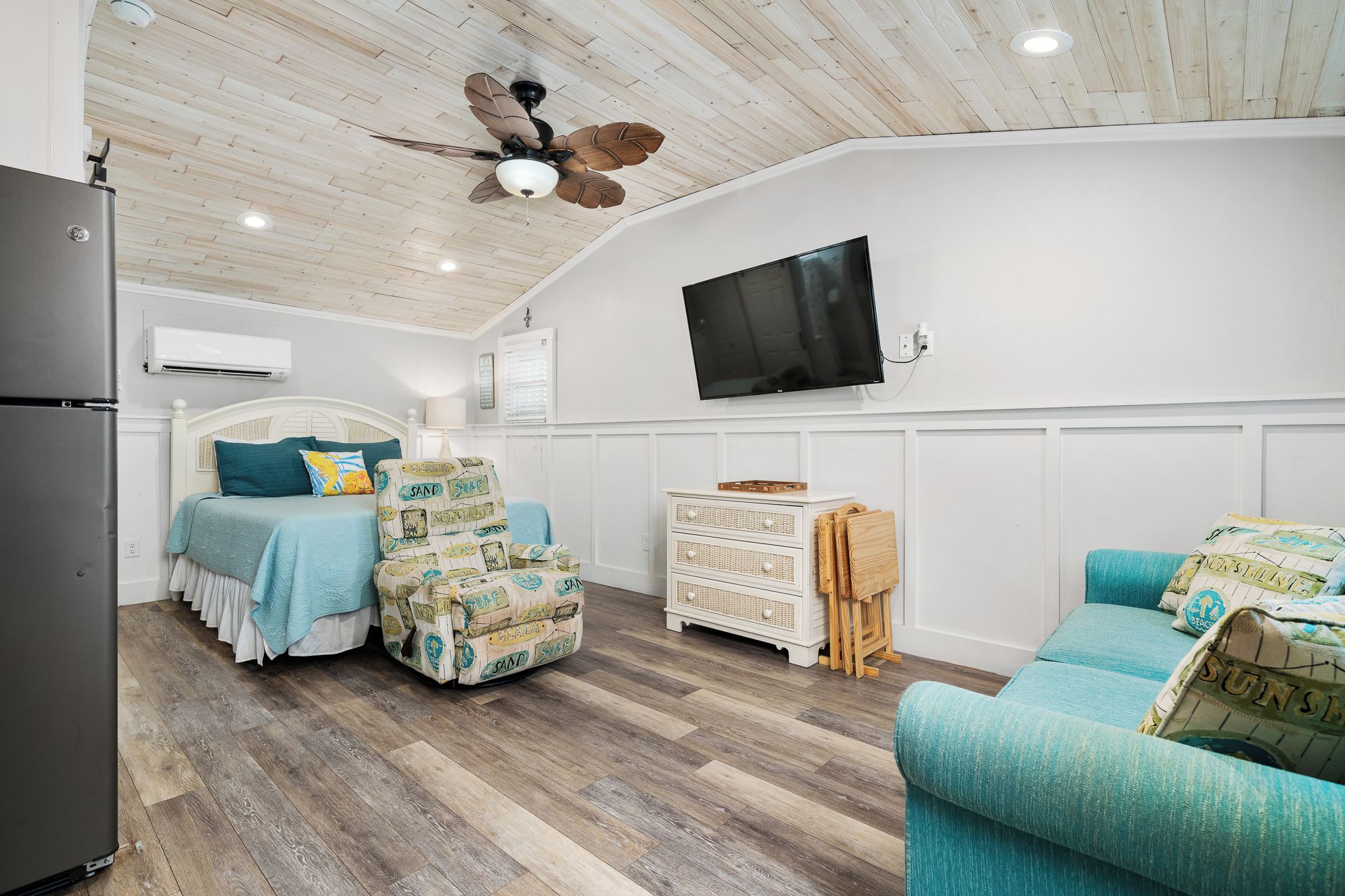 Un dormitorio con cama, cómoda, televisor y ventilador de techo.