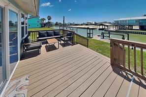 A wooden deck with outdoor furniture, a view of a marina, and a building with a blue exterior. - Hideaway at Redhead Road by Miss Kitty’s (Rockport)