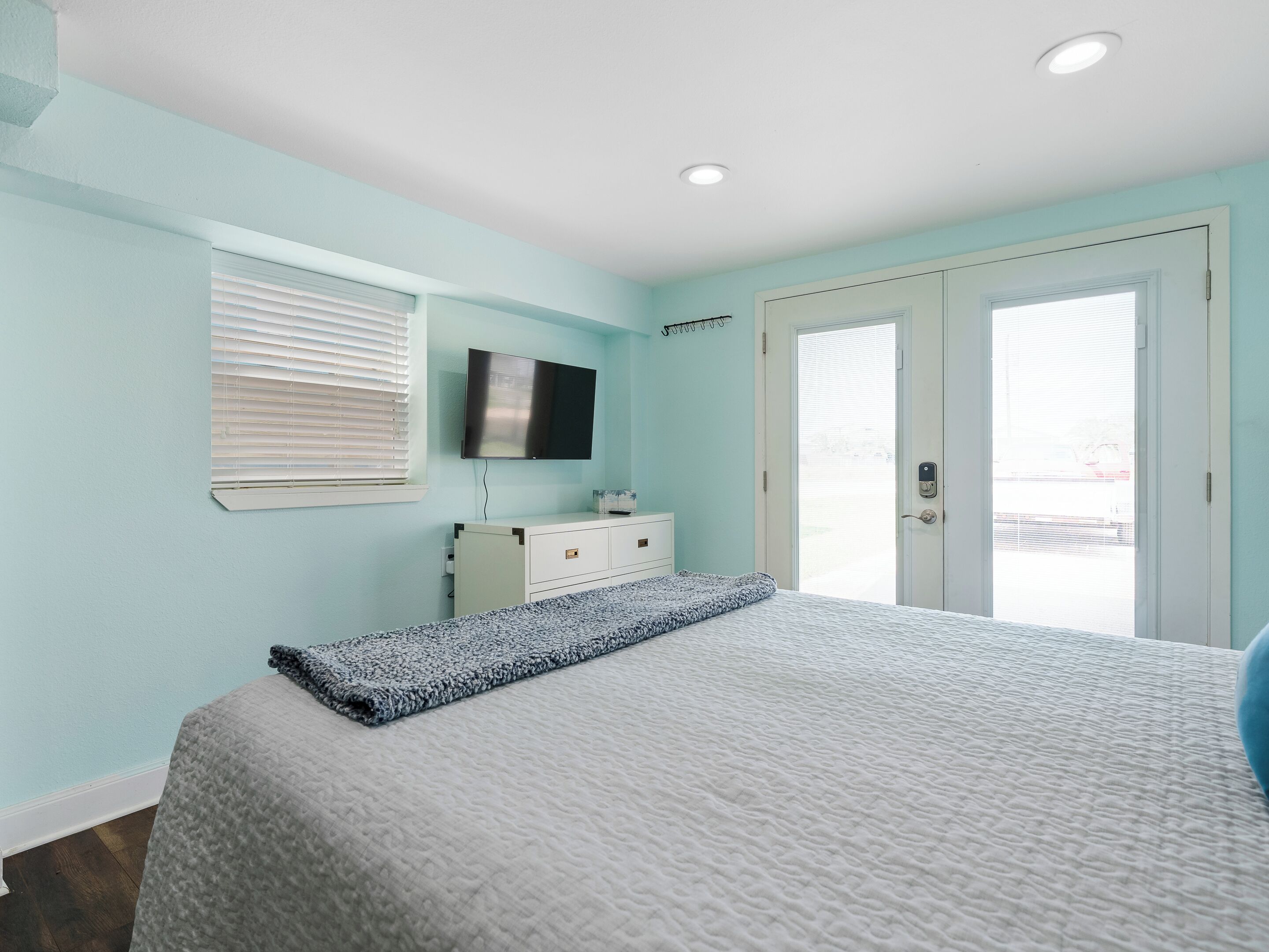 A bedroom with a bed, a TV mounted on the wall, a dresser, and a door leading to a balcony.
