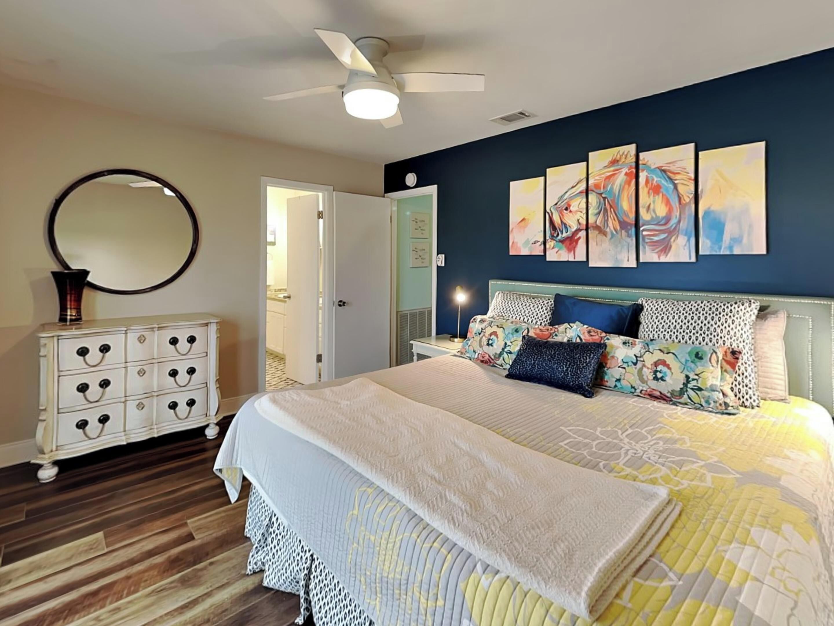 A bedroom with a bed, a dresser, a mirror, and artwork on the wall.