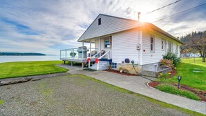 A white house with a covered porch, a small garden, and a view of the water. - Oak Bay Beach House in Port Hadlock (Port Hadlock-Irondale)
