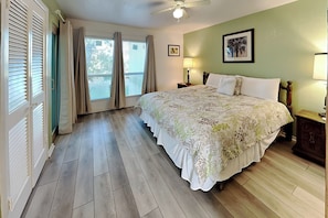 A bedroom with a bed, curtains, a ceiling fan, a nightstand, a lamp, and a framed picture on the wall.