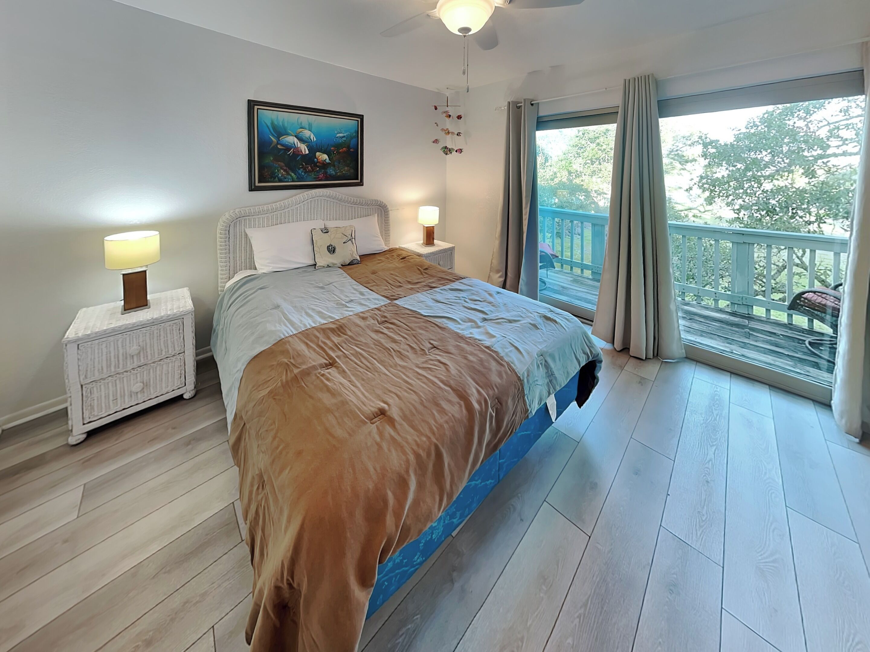 A bedroom with a bed, nightstands, a ceiling fan, a painting, and a balcony view.