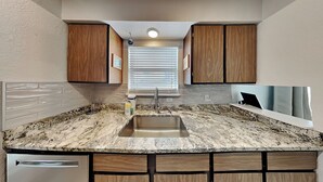 A kitchen with granite countertops, wooden cabinets, a stainless steel sink, and a built-in dishwasher. - A Bay From It All by Miss Kitty’s (Rockport)