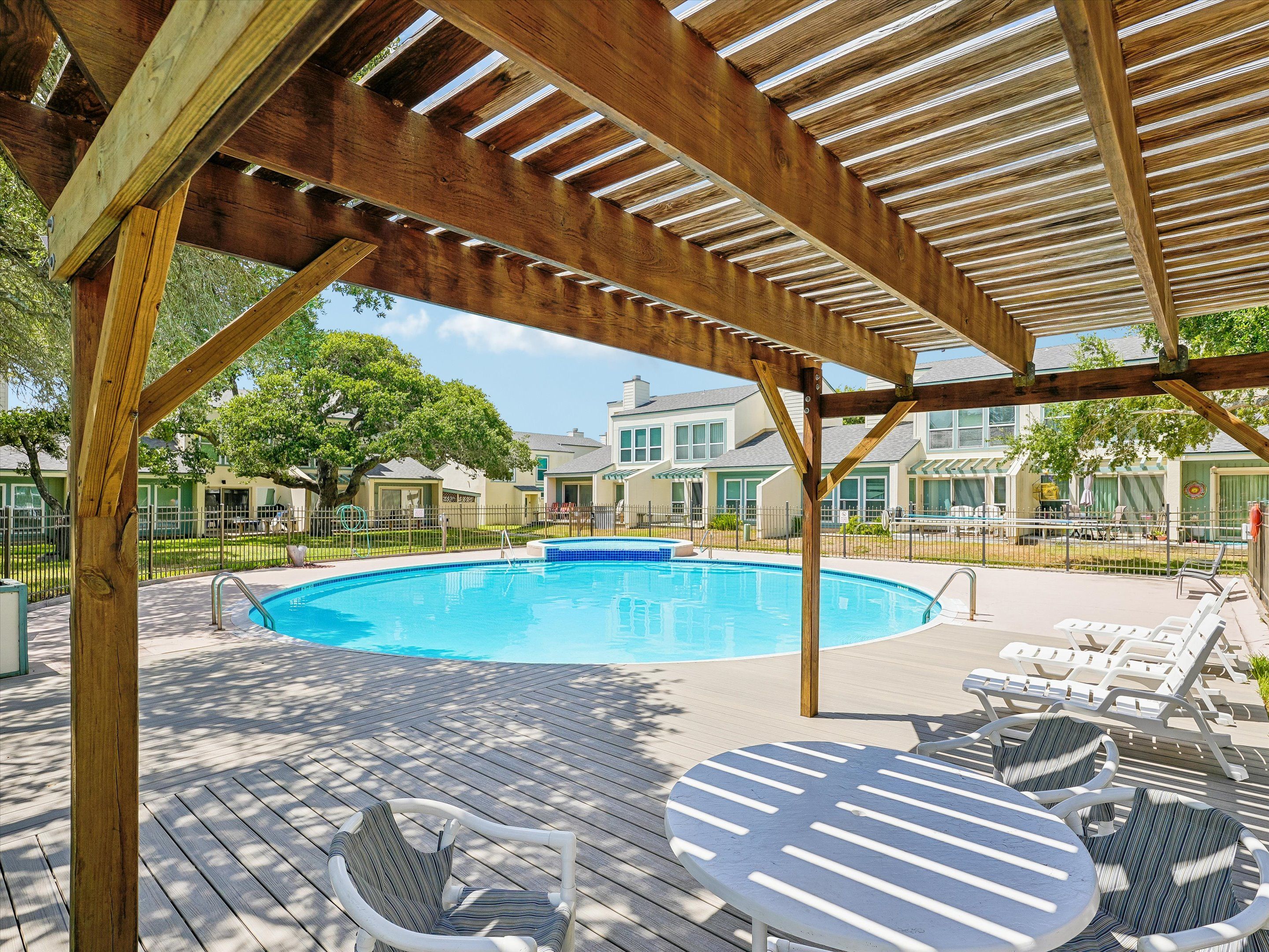 A wooden deck with a pool, lounge chairs, and a covered area.