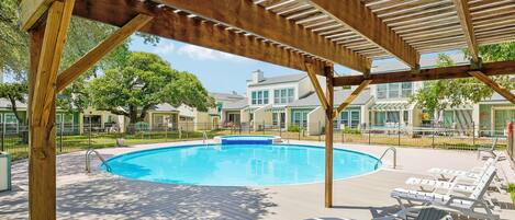 A wooden deck with a pool, lounge chairs, and a covered area.