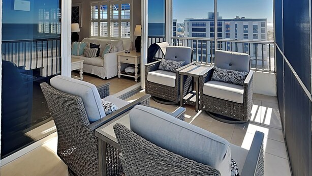 A balcony with wicker furniture, a sofa, and a table. - Estero Island Beach Villas by Distinctive Beach Rentals (Fort Myers Beach)