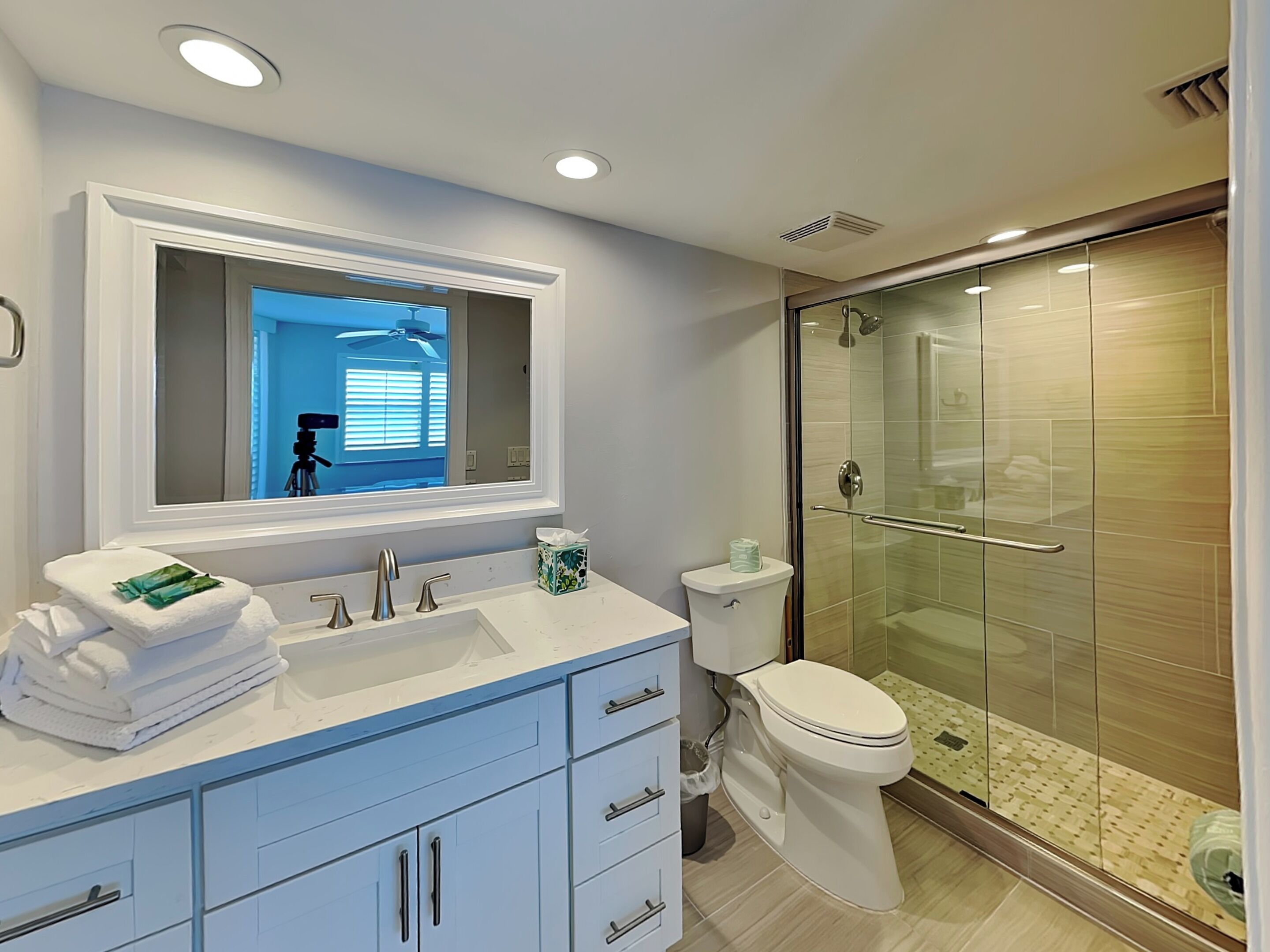 Un baño moderno con un lavamanos blanco, armarios azules, un inodoro y una ducha con cerramiento de vidrio.