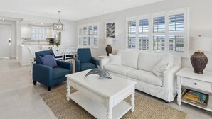A spacious living room with a white sofa, blue armchairs, a white coffee table, and a ceiling fan. - Estero Island Beach Villas by Distinctive Beach Rentals (Fort Myers Beach)