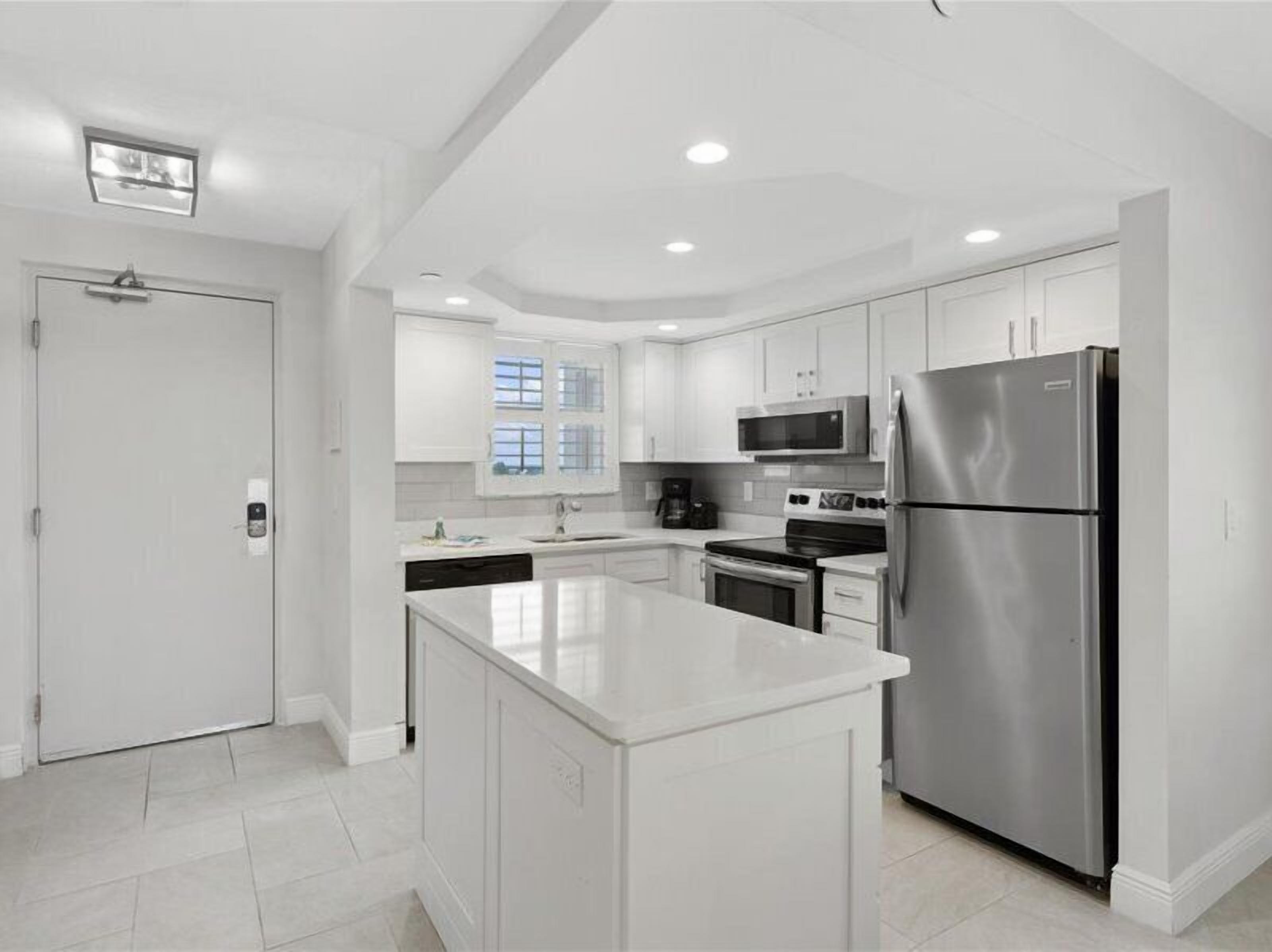 A modern kitchen with white cabinetry, stainless steel appliances, and a large island.