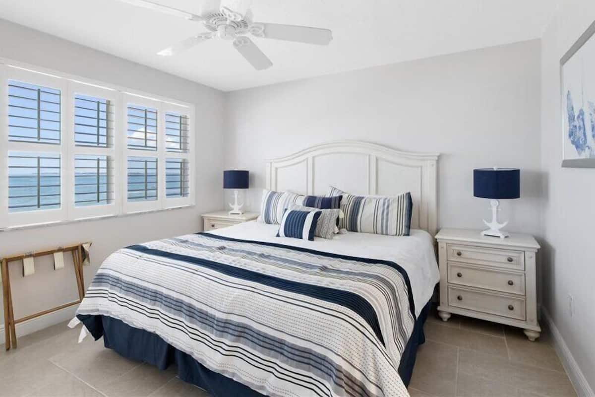 A bedroom with a bed, two bedside tables, a ceiling fan, and a window with blinds.