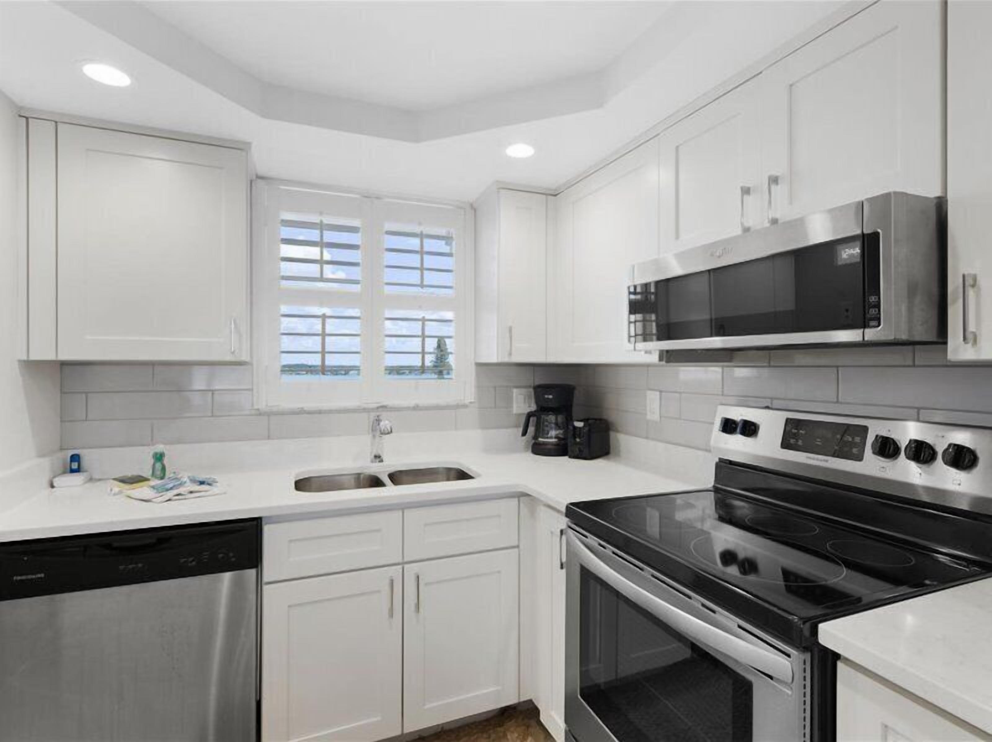 A modern kitchen with white cabinets, a stainless steel dishwasher, a double sink, a coffee maker, a microwave, and a stove.