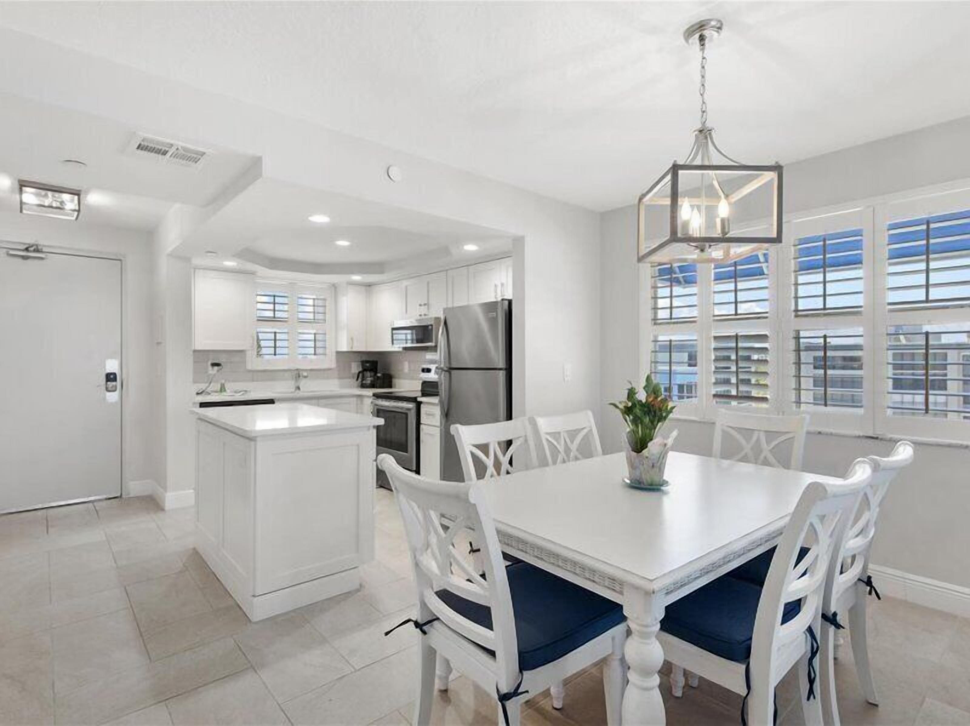 A modern kitchen with white cabinetry, a central island, and a dining area with white chairs and a table.