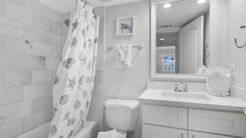 A modern bathroom with a shower curtain featuring sea creatures, a toilet, a sink with a mirror above it, and a small framed picture on the wall.