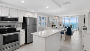 A modern kitchen with stainless steel appliances, a large island, and a view of the ocean. - Estero Island Beach Villas by Distinctive Beach Rentals (Fort Myers Beach)
