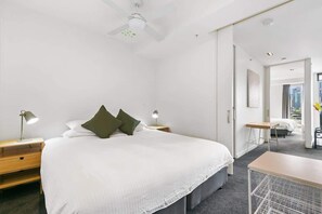 Moderni hotellihuone, jossa on suuri sänky, yöpöydät lampuineen, työpöytä ja näkymä kaupunkiin.