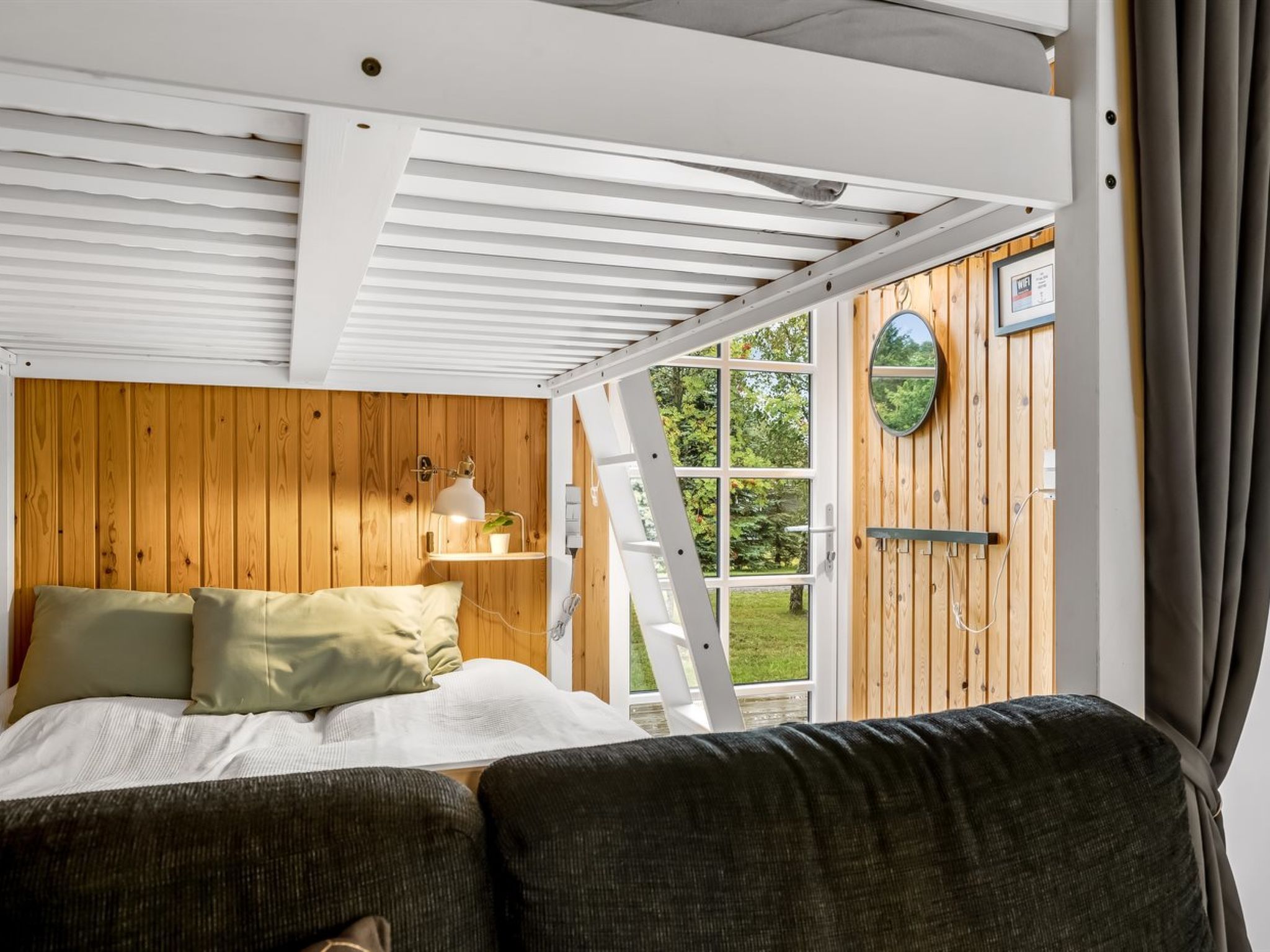 A bedroom with a bed, a bedside table, a lamp, a window, and a view of greenery outside.