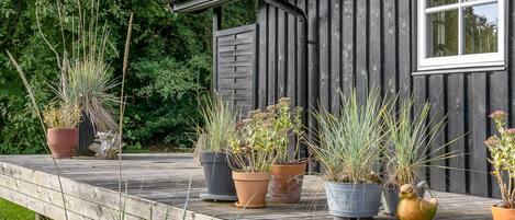 En træterrasse med plantekasser og et hus med et vindue og tagrende.