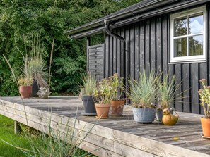 Eine Holzterrasse mit Topfpflanzen und ein Haus mit Fenster und Regenrinne.