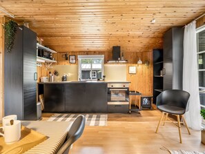 Eine moderne Küche mit Holzbalkendecke, einer zentralen Kochinsel und einem Essbereich mit Stuhl und Tisch.