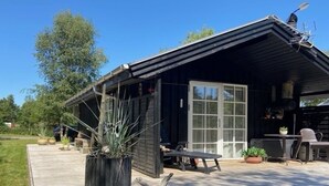 A small wooden cabin with a deck, a large window, and a grill area.