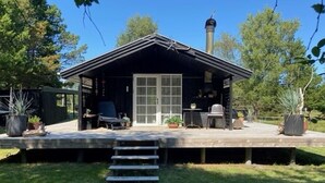 A cabin with a deck, a chimney, and a door leading to a covered porch.