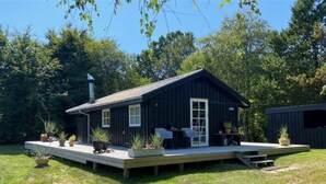A small wooden cabin with a deck, surrounded by greenery.