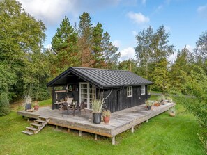Eine Holzhütte mit einer Veranda, umgeben von Bäumen und viel Grün.