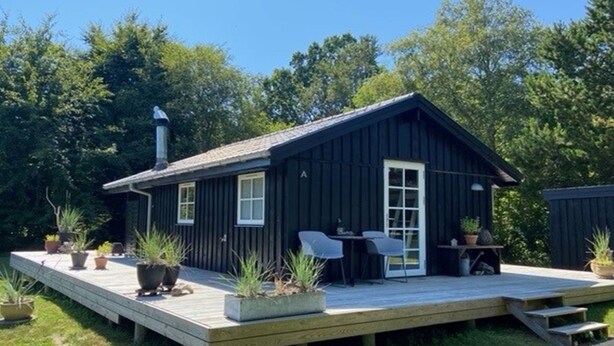 A small, dark wooden cabin with a deck, a chimney, and a door.