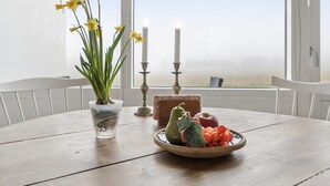 A round wooden table with a white chair, a vase with yellow flowers, a candle holder, and a bowl of fruit.