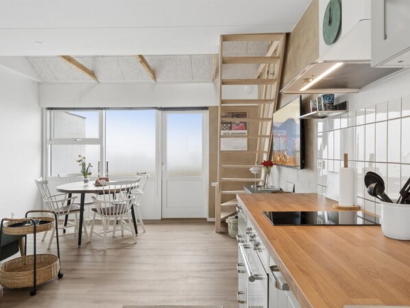 A modern kitchen with a wooden countertop, white cabinets, and a dining area with a table and chairs.