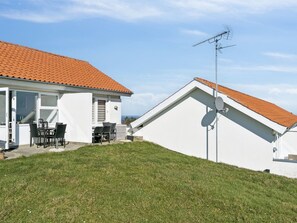 Uma casa com telhado de telhas vermelhas, antena parabólica e um pátio com cadeiras.