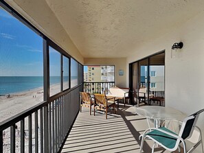 Un balcon avec vue sur la plage et l’océan. On y trouve des chaises et une table en bois, ainsi que des sièges.