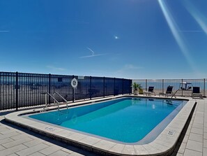 Une piscine entourée d’une clôture noire, avec le soleil qui brille et un ciel dégagé.