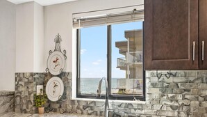 A kitchen with a large window, a marble countertop, and a view of the ocean. - Arie Dam 404 by Ryson Vacation Rentals (Madeira Beach)