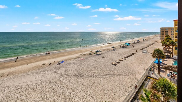 A beach with a pool area, palm trees, and a building with balconies. - Arie Dam 404 by Ryson Vacation Rentals (Madeira Beach)
