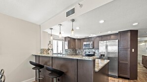 A modern kitchen with dark wood cabinets, stainless steel appliances, a marble countertop, and pendant lighting. - Arie Dam 404 by Ryson Vacation Rentals (Madeira Beach)