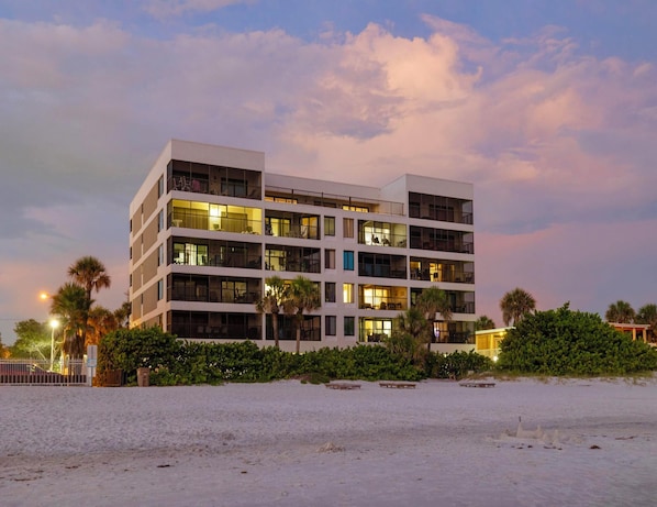 Een meerlaags hotel met balkons, gelegen aan een zandstrand.