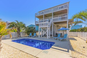 A two-story building with a pool, outdoor seating, and a wooden deck. - Gorgeous 2nd Row Oceanview 4 Bedroom Home with Large Salt Water Pool (Oak Island)