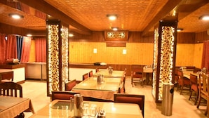A restaurant with wooden panel walls, patterned ceiling, and traditional decor. Tables are set with glass tops and metal pitchers. - Hotel Akbar  (Srinagar)