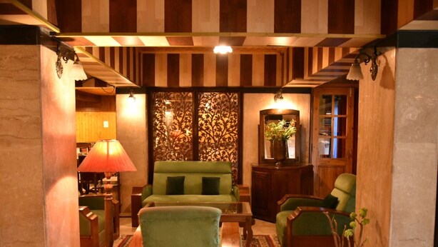A cozy living room with striped wooden beams, a green sofa, and a coffee table. - Hotel Akbar  (Srinagar)